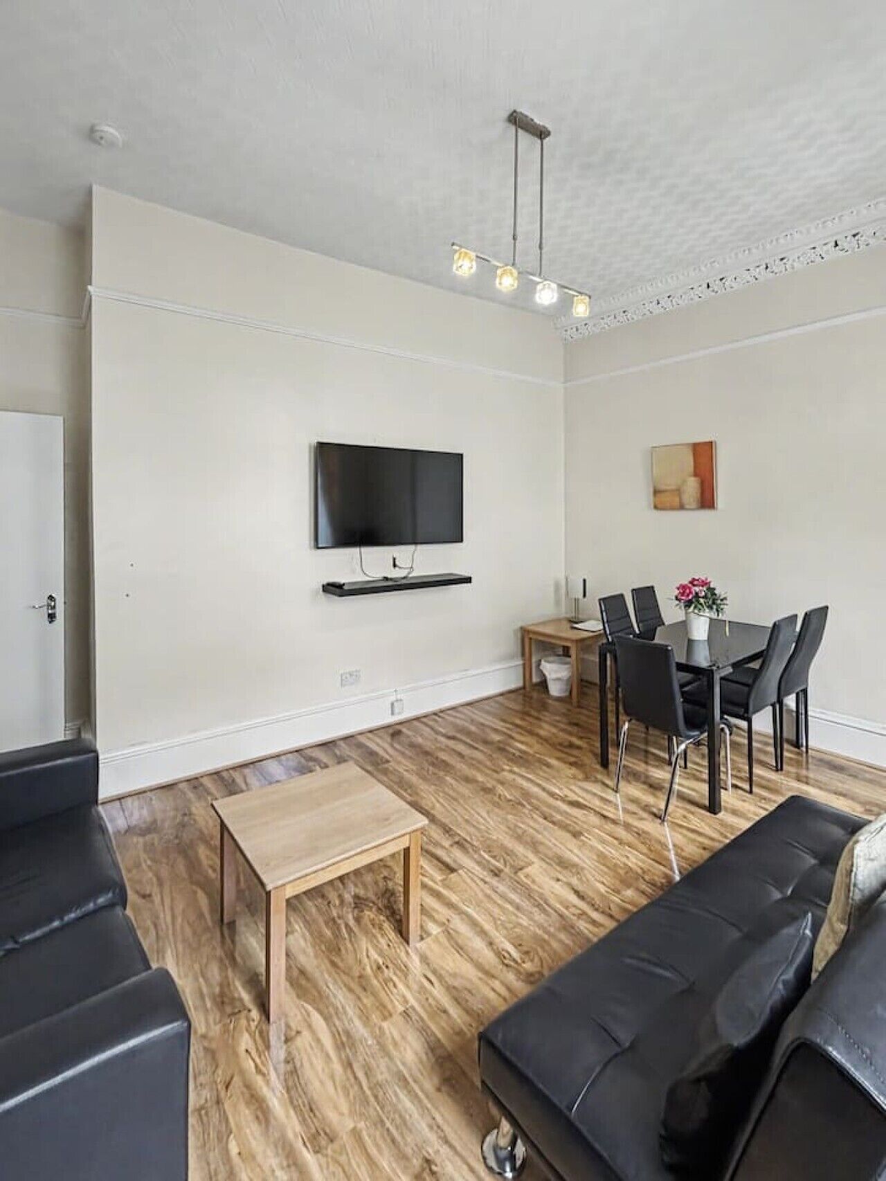 A modern living room with a flat-screen TV, a dining table with chairs, a coffee table, and a sofa.
