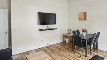 A modern living room with a flat-screen TV, a dining table with chairs, a coffee table, and a sofa.