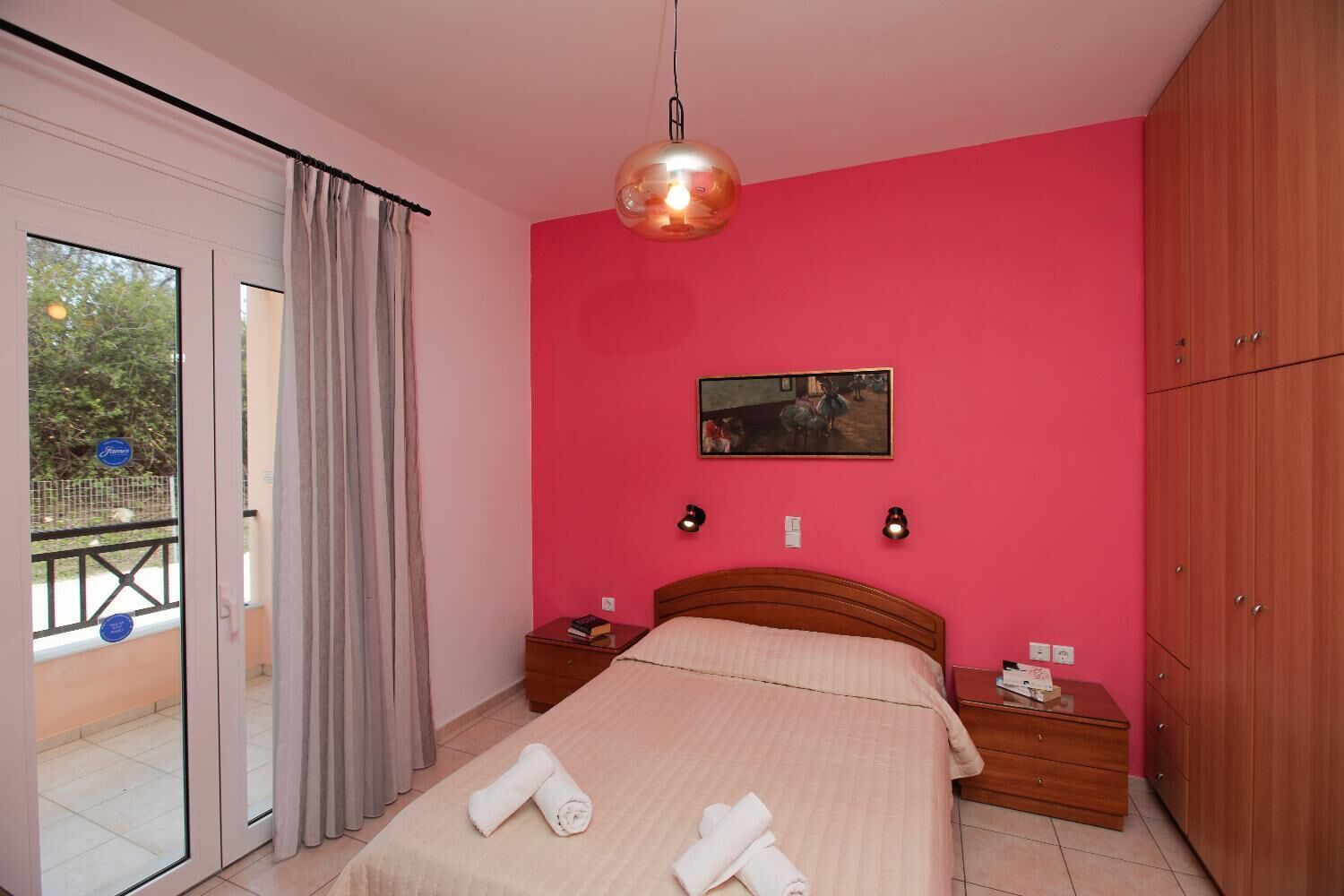 A bedroom with a bed, bedside tables, a hanging light fixture, a painting, and a wardrobe.