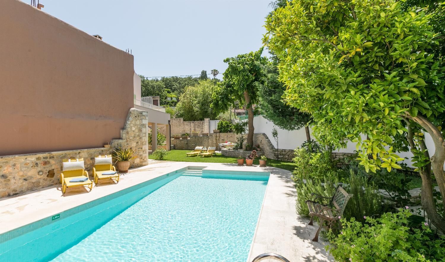 A swimming pool with lounge chairs, surrounded by greenery and stone walls.
