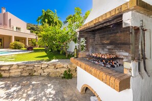 Un espace barbecue extérieur avec un mur en pierre et une piscine en arrière-plan.