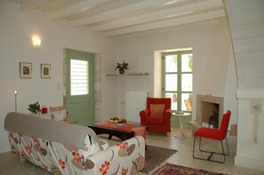 Ein Wohnzimmer mit einer Couch, einem roten Sessel, einem kleinen Tisch mit Obstschale, einem Kamin und einer grünen Tür.