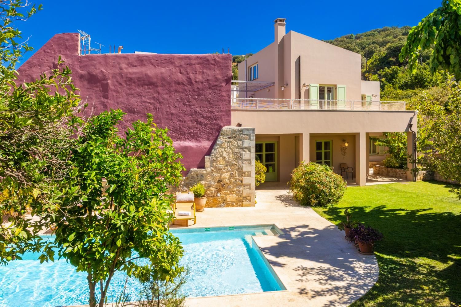 Una casa moderna con piscina, un muro de piedra y un jardín cuidado.