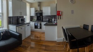 A modern kitchen with white cabinets, a microwave, and a stove. There is a dining area with a black table and chairs.