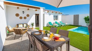 Ein Essbereich im Freien mit einem Tisch für zwei Personen, umgeben von Korbstühlen, einem Pool und Liegestühlen.