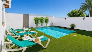 Ein Pool mit Kunstgrasanlage, Liegestühlen und Topfpflanzen.