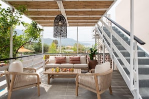 Ein überdachter Außenbereich mit einer Sitzecke, inklusive Sofa und Stühlen, einem Tisch mit Speisen sowie einer Treppe.