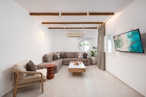 Ein modernes Wohnzimmer mit einer Eckcouch, einem runden Couchtisch, einem Korbstuhl und einem flachbildfernseher an der Wand.