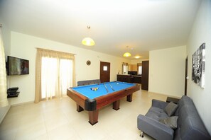 Un salon comprenant une table de billard, un canapé, un téléviseur et un coin cuisine.