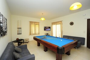 Ein Billardtisch mit blauer Spielbahn, ein graues Sofa, ein Fernseher und eine Uhr an der Wand.