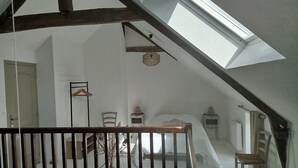 An attic bedroom with a sloped ceiling, a wooden railing, a bed, a chair, and a small table. - A vacation rental in the heart of Morbihan, nestled between land, river, and ocean! A guaranteed chance to recharge! (Saint-Dolay)