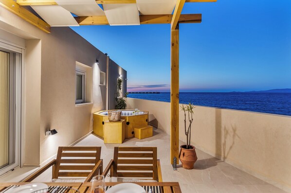 A balcony with a wooden table, chairs, a small sofa, and a potted plant.