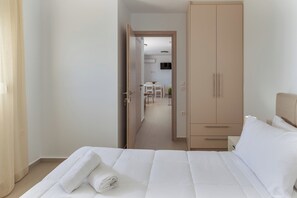 A hotel room with a bed, a wardrobe, and a view into the dining area.