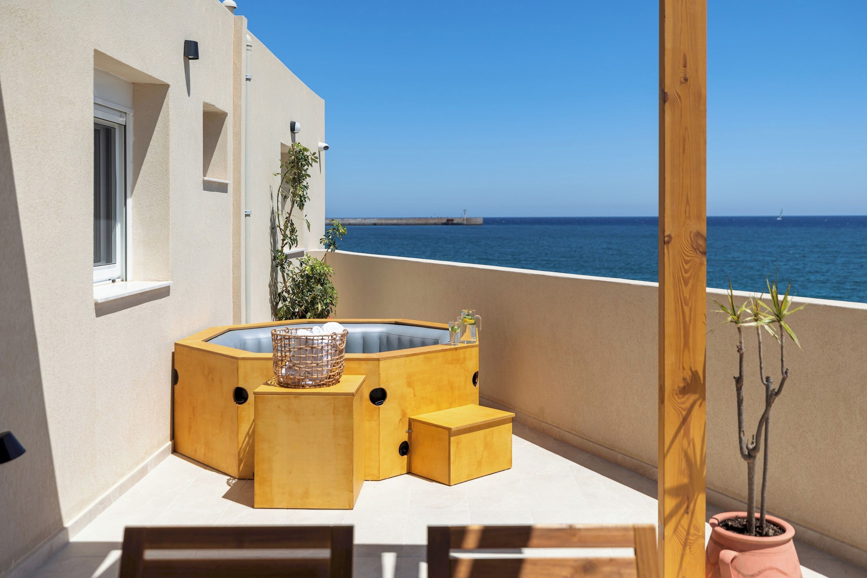 A wooden outdoor seating area with a hot tub, potted plants, and a view of the sea.