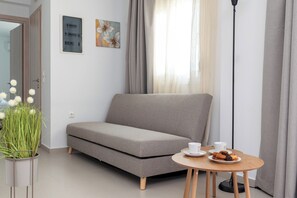 Ein modernes Wohnzimmer mit einem grauen Sofa, einem kleinen runden Tisch mit Tasse und Gebäck, einer Topfpflanze und einer Steckdose an der Wand.