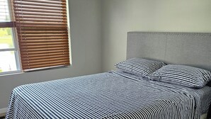 Ein Schlafzimmer mit Bett, Kopfteil und Fenster mit Jalousien.