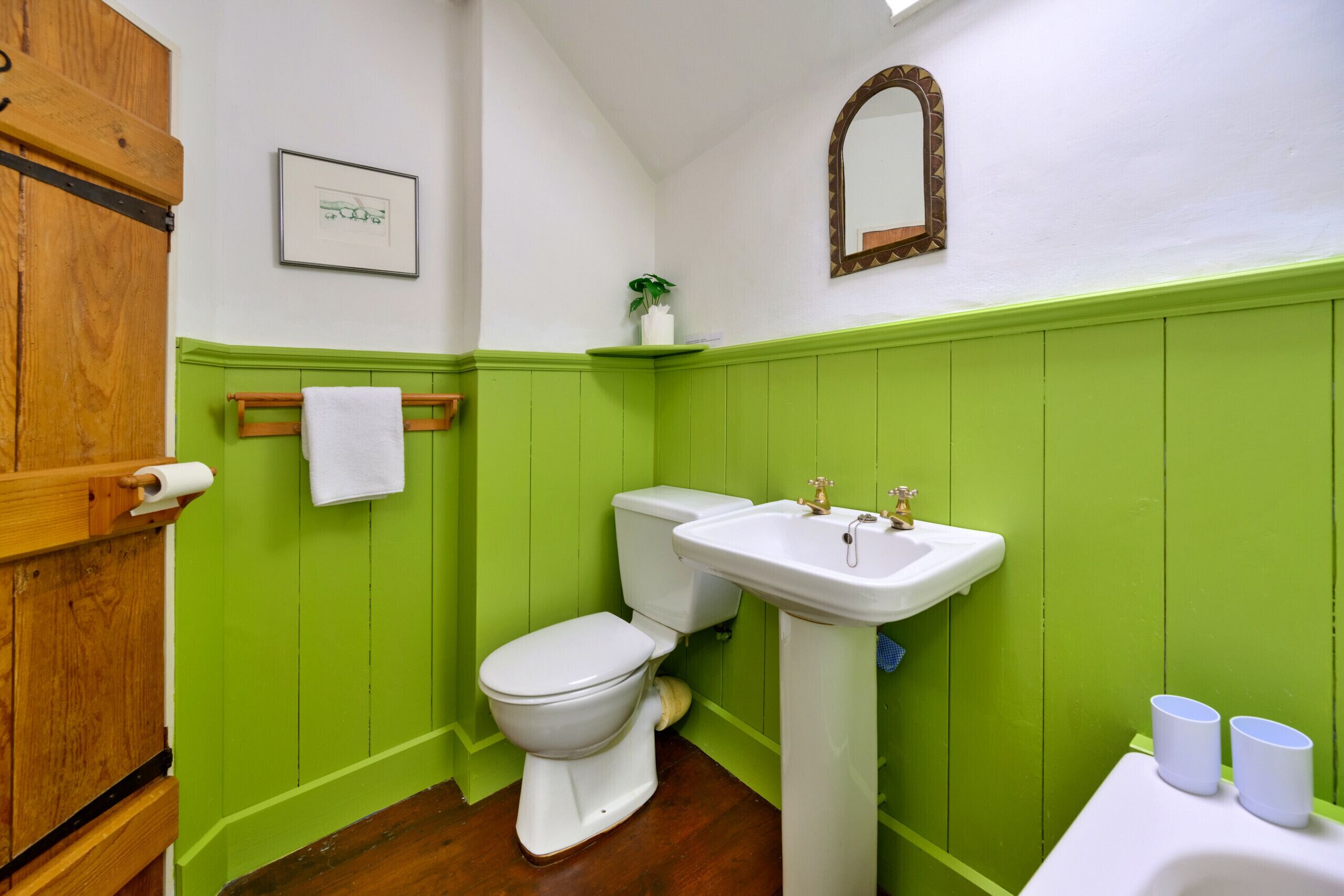 A bathroom with a toilet, sink, and green wall paneling.