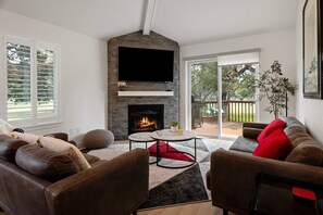 A living room with a fireplace, a flat-screen TV, and a view of the outdoors.