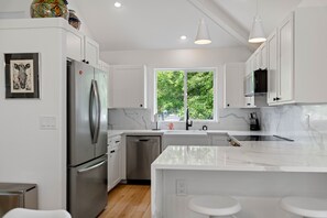 A modern kitchen with white cabinetry, stainless steel appliances, a marble countertop, and a window with a view of greenery. - Eagle Crest Golf Views & Amenities, 1 Pet Free (Redmond)
