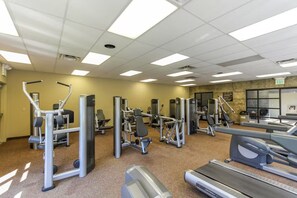 A gym with various exercise machines, a treadmill, and a mirrored wall.