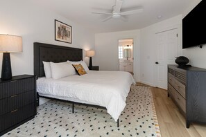 A bedroom with a bed, two bedside tables, a ceiling fan, a TV, and a door leading to a bathroom. - Eagle Crest Golf Views & Amenities, 1 Pet Free (Redmond)