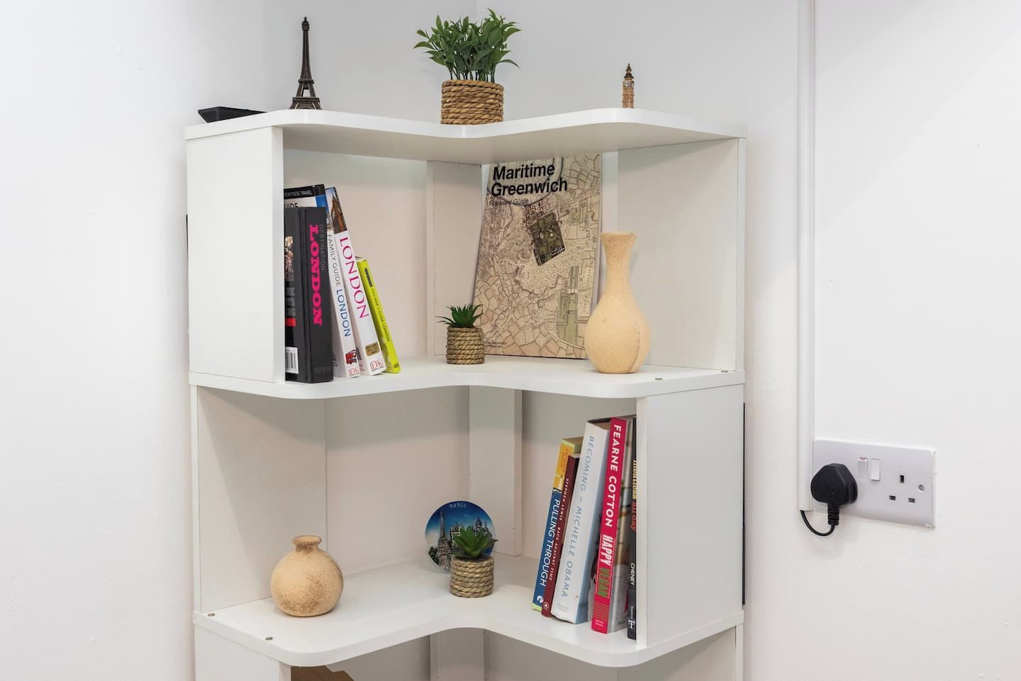 Estante branca com livros, um mapa e objetos decorativos.