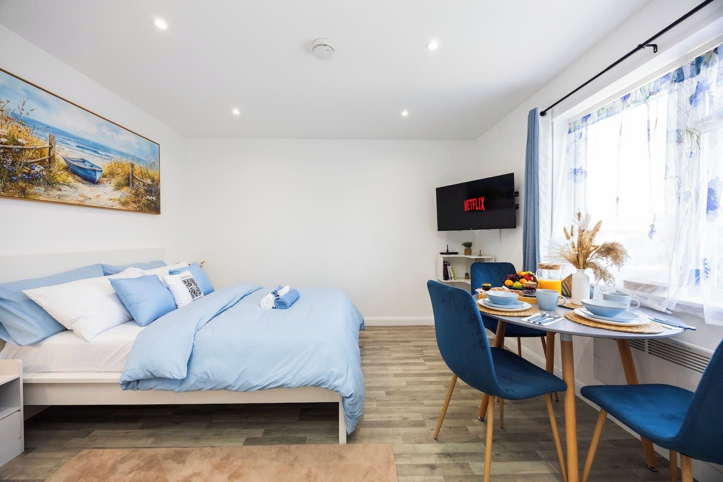 Un dormitorio moderno con cama, un escritorio con provisiones para el desayuno, un televisor y un cuadro en la pared.