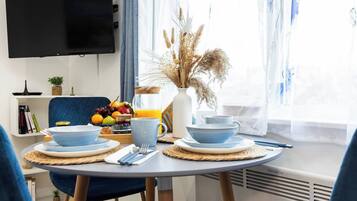 Uma área de refeições com mesa posta para o café da manhã, incluindo pratos, xícaras e uma cesta de frutas.