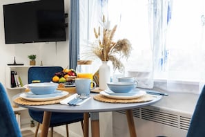 Uma área de refeições com mesa posta para o café da manhã, incluindo pratos, xícaras e uma cesta de frutas.