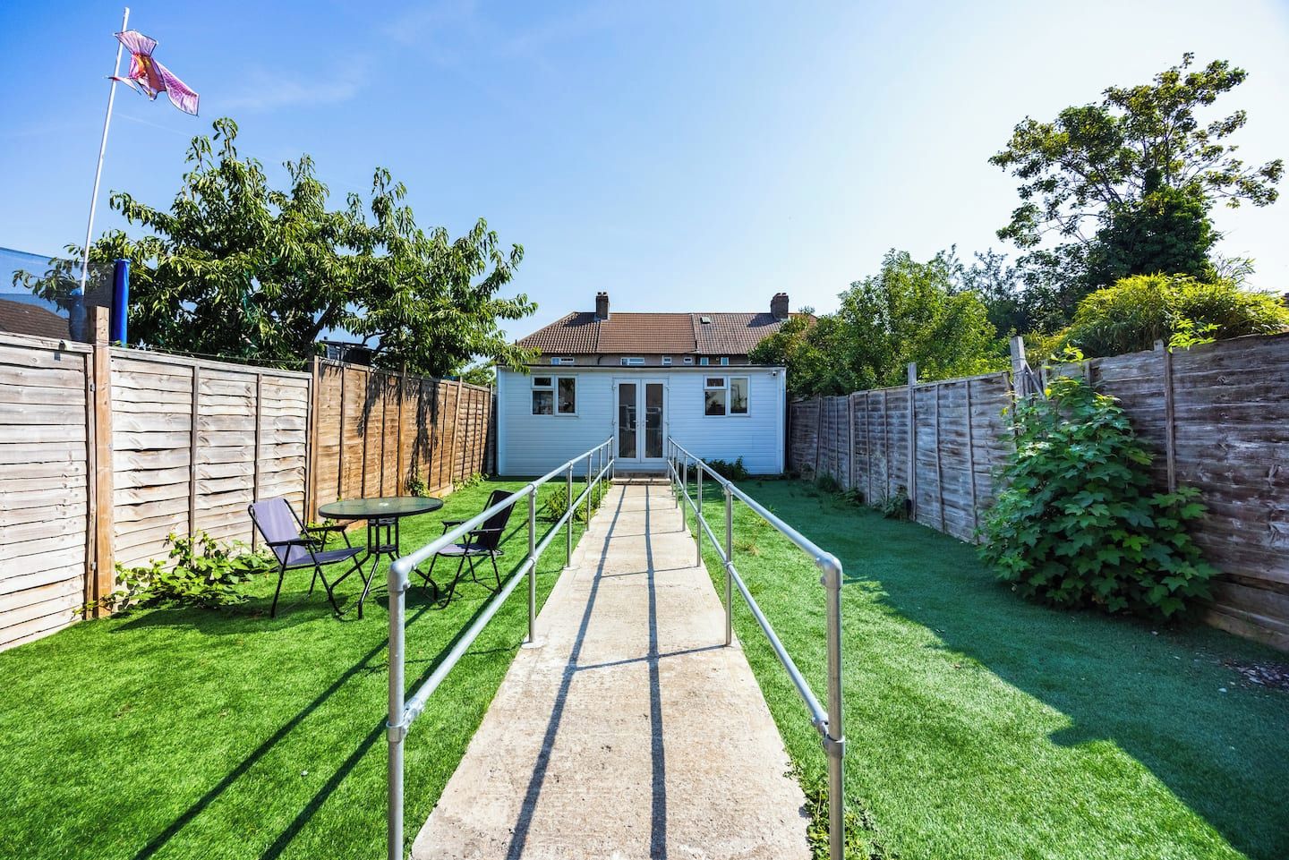 A backyard with a concrete pathway leading to a house, surrounded by wooden fences and greenery.