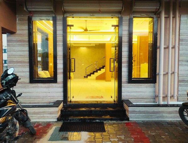 A building entrance with a glass door, a staircase inside, and a parked motorcycle outside.