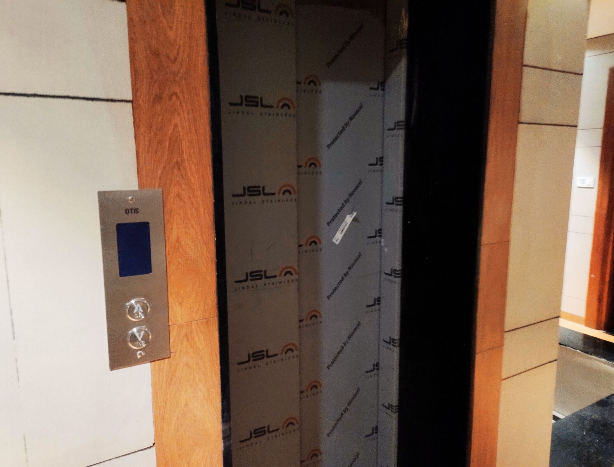 L’intérieur d’un ascenseur, avec un panneau de commande portant l’inscription « OTIS » et un mur orné du logo « JSL ».