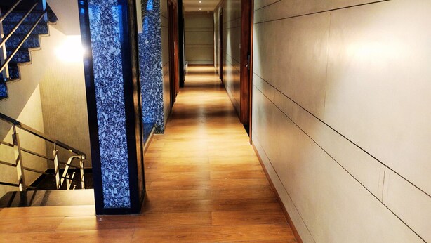 Un pasillo de hotel moderno con suelo de madera, una columna de mármol y una escalera.