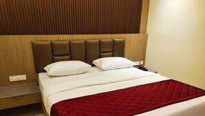 Habitación de hotel con una cama, dos almohadas, una colcha roja, un cabecero de madera, una mesita de noche y un teléfono.