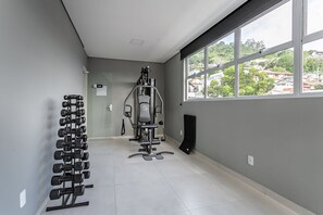 A gym with exercise equipment, a dumbbell rack, and a window with a view of buildings. - New studio near Beiramar Shopping #HKS14 (Florianópolis)