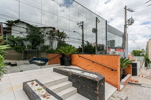 Ein modernes Gebäude mit Glasfassade, Außenbereich mit Sitzgelegenheiten und einer Backsteinmauer mit Stufen zu einem Dachgarten.