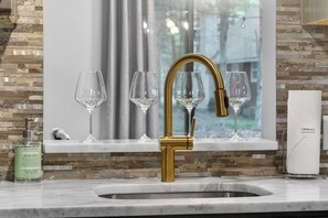 Ein Badezimmer mit goldfarbenem Wasserhahn, Marmorplatte und einem Fenster mit Blick auf Bäume.