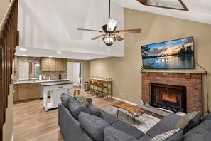 Ein modernes Wohnzimmer mit Kamin, Fernseher und Essbereich, im Hintergrund eine Küche.