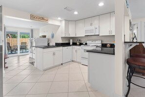 A modern kitchen with white cabinets, a black countertop, and a dining area with a table and chairs. - Chuck & Margies Coastal Escape (Cortez)