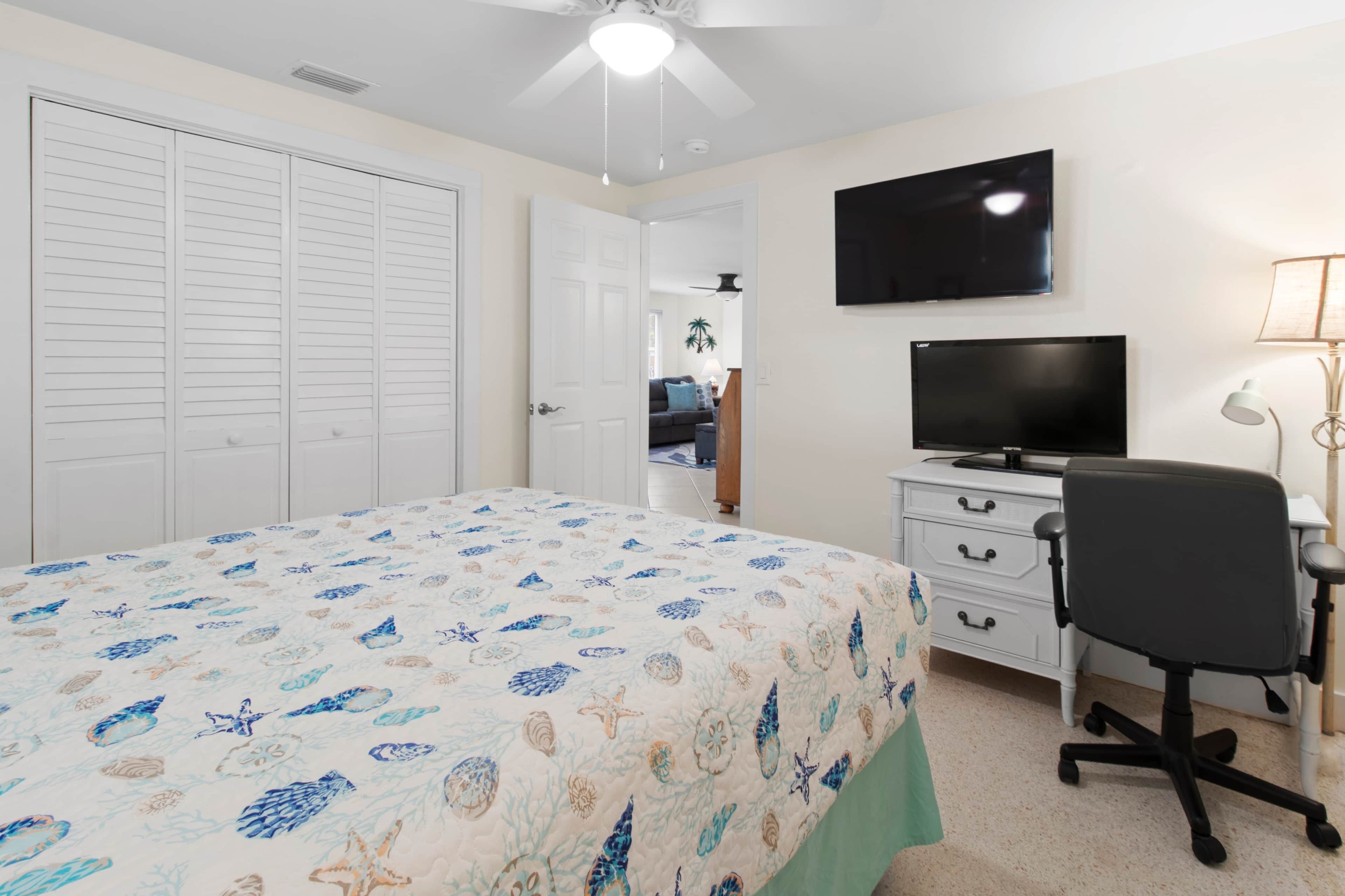 A bedroom with a bed, a desk, a chair, a TV, and a closet.