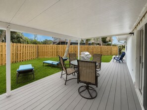 Eine überdachte Terrasse mit Tisch, Stühlen, einem Grill und einer Liege am Pool.