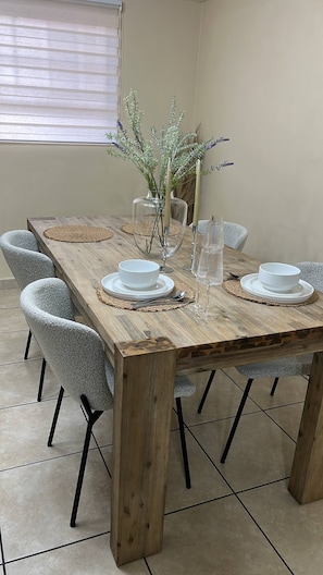 Une table à manger en bois, avec de l’assiette blanche, des verres transparents et un vase décoré de verdure.