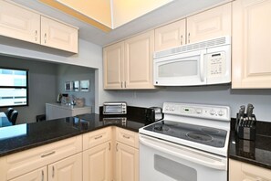 Une cuisine avec des meubles blancs, un four à micro-ondes, une cuisinière, un grille-pain et un bloc à couteaux.