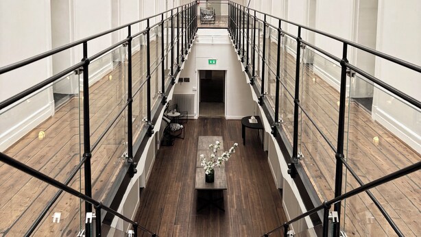 A hotel corridor with a skylight, glass railings, and wooden floors.