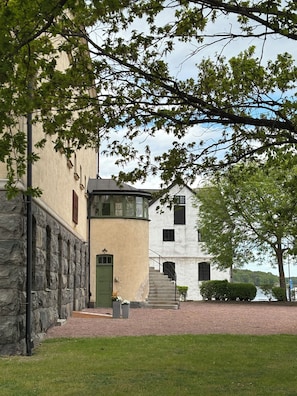 A building with a stone facade, a green door, and a staircase leading to a white building with black shutters. - Maj på Kronohäktet Karlskrona (Karlskrona)
