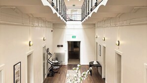 A spacious corridor with a high ceiling, wooden flooring, and a central table with a vase of flowers.