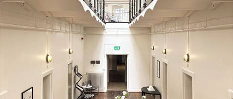 A spacious corridor with a high ceiling, wooden flooring, and a central table with a vase of flowers.