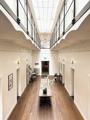 A spacious corridor with a high ceiling, wooden flooring, and a central table with a vase of flowers. - Maj på Kronohäktet Karlskrona (Karlskrona)