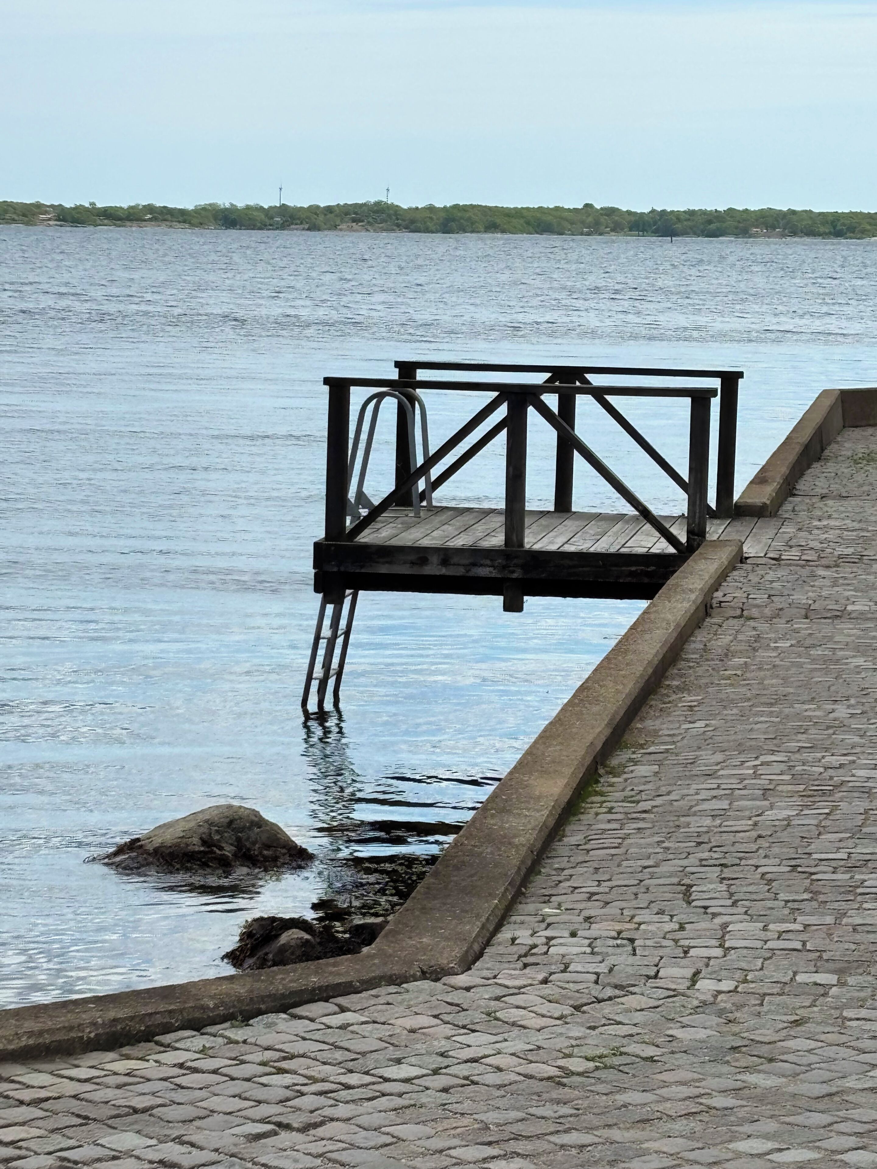 Een houten steiger die zich uitstrekt over kalm water, met een verhard pad ernaast.