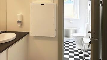 Et badeværelse med en hvid vask, et hvidt skab, gulv i sort og hvid tern og udsigt til en balkon med et hvidt toilet.